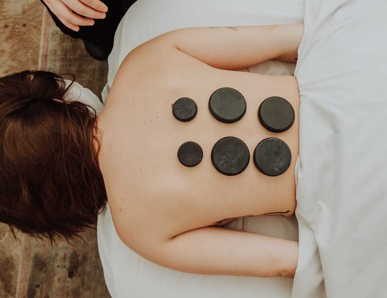 Person receiving hot stone therapy on their back in a spa setting.