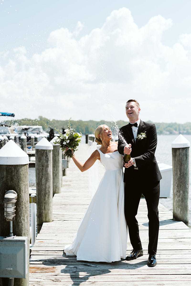 Bride and groom celebrating with champagne on a sunny dock.