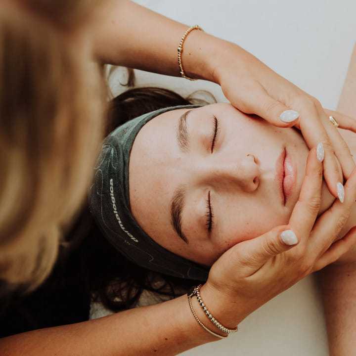 Facial massage with hands gently cradling a woman's head, eyes closed, peaceful expression.