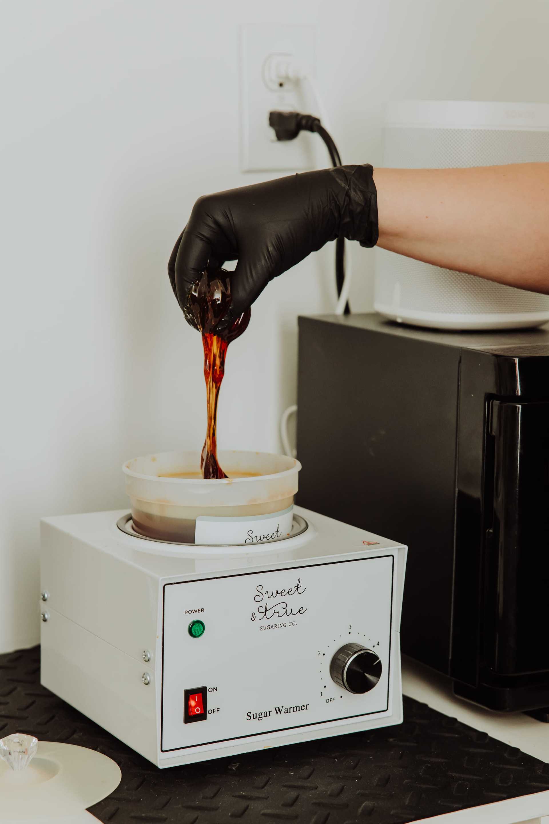 Hand in glove holding melted sugar over a warmer in a beauty salon setting.