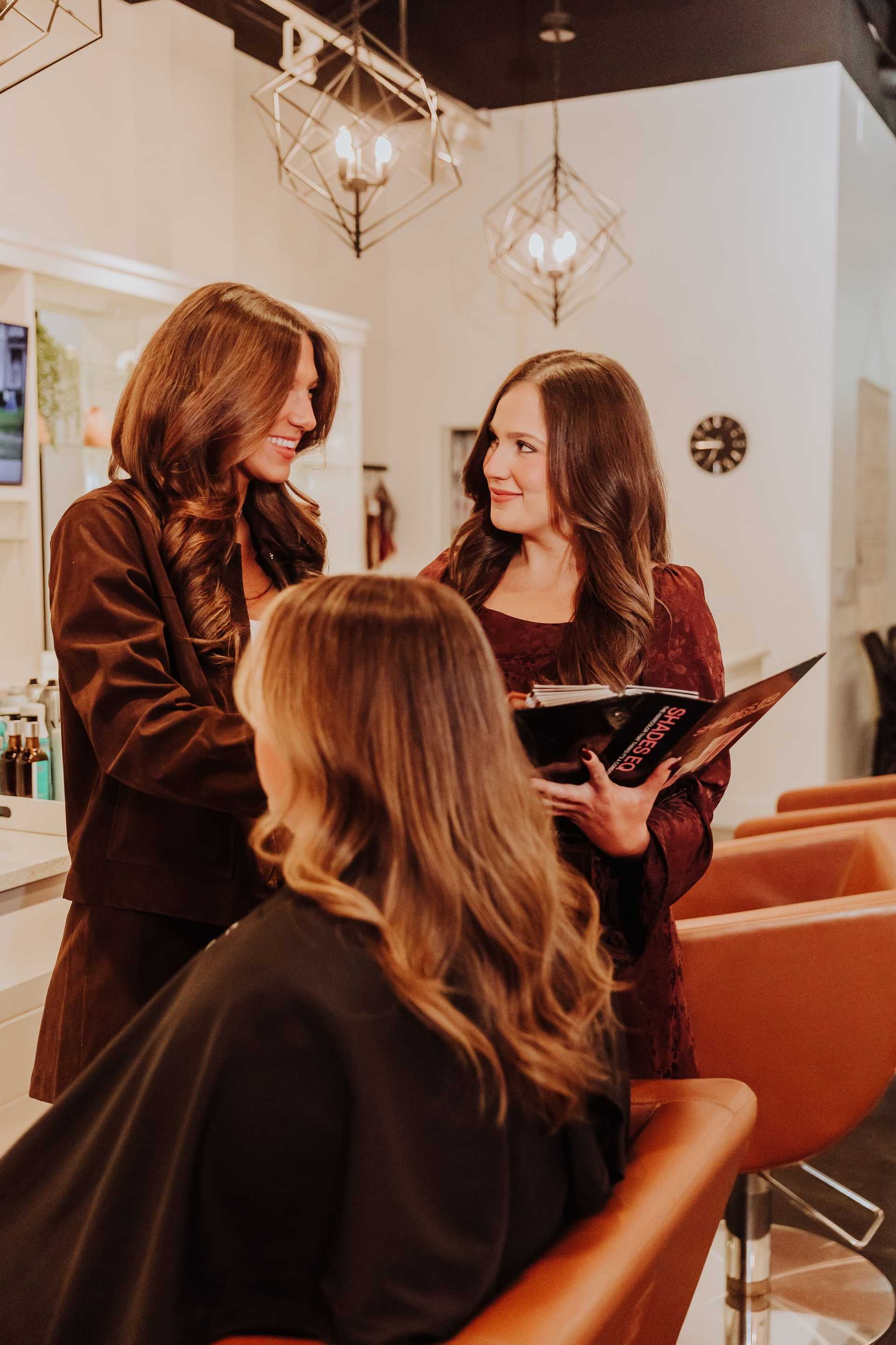 Women chatting in a salon, one seated getting a haircut, while others discuss hairstyling options.